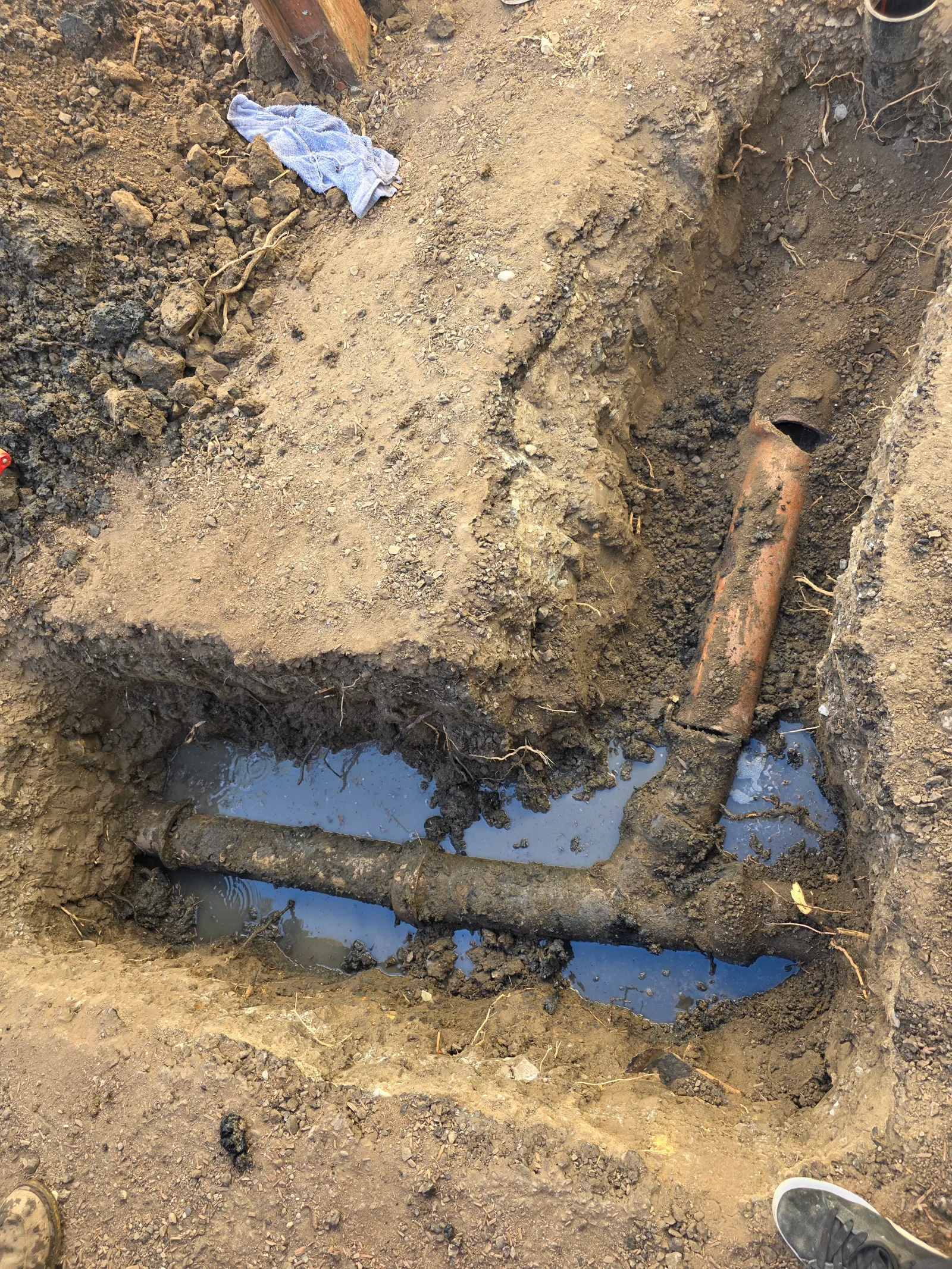 Underground gas line installation in excavated trench with corroded metal pipes and water pooling