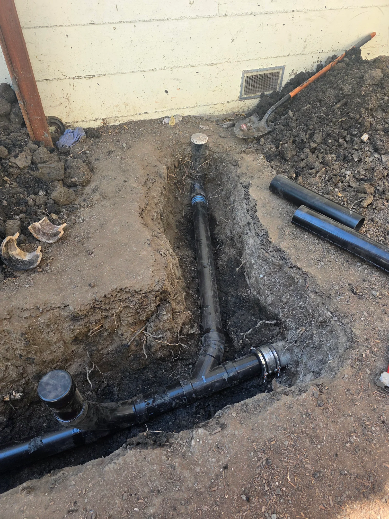 Black perforated drain pipe with blue couplings installed in foundation trench with soil backfill