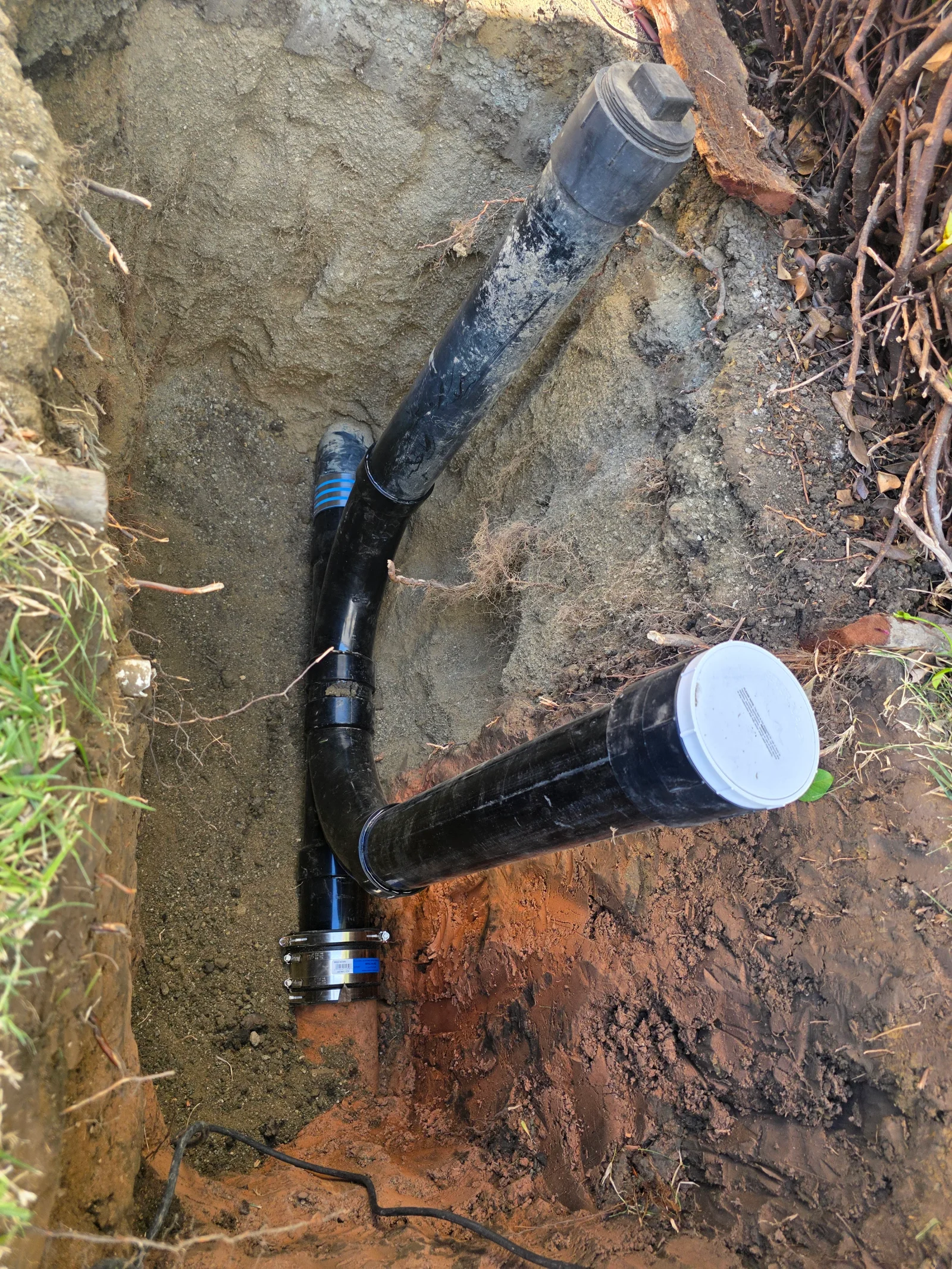 Black polyethylene gas pipe with blue stripe, compression fittings, and white cap installed in underground trench